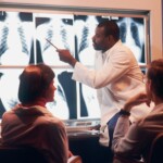 a man in a white lab coat pointing to an x - ray